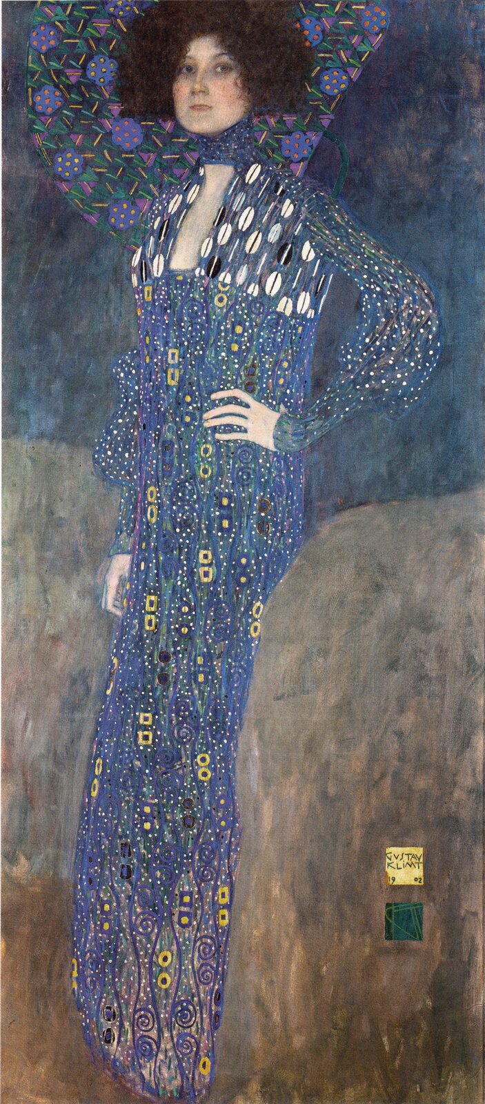 Obraz Gustava Klimta „Portret Emilie Flöge” przedstawia stojącą kobietę w długiej, bogato zdobionej sukni w odcieniach błękitu, fioletu i zieleni. Kobieta ma krótkie, ciemne, puszyste włosy i patrzy wprost na widza. Suknię pokrywają liczne geometryczne i spiralne ornamenty w kolorze żółtym, niebieskim, białym i czarnym. Wokół głowy i ramion rozciąga się dekoracyjny wzór z fioletowych kwiatów, zielonych liści i geometrycznych form. Tło jest ciemne i stonowane, kontrastujące z intensywnymi barwami stroju.