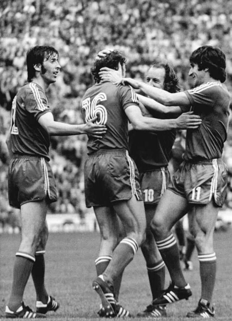 Zdjęcie przedstawia czterech polskich piłkarzy na murawie stadionu. Mężczyźni obejmują piłkarza z numerem szesnaście na koszulce. Cieszą się.