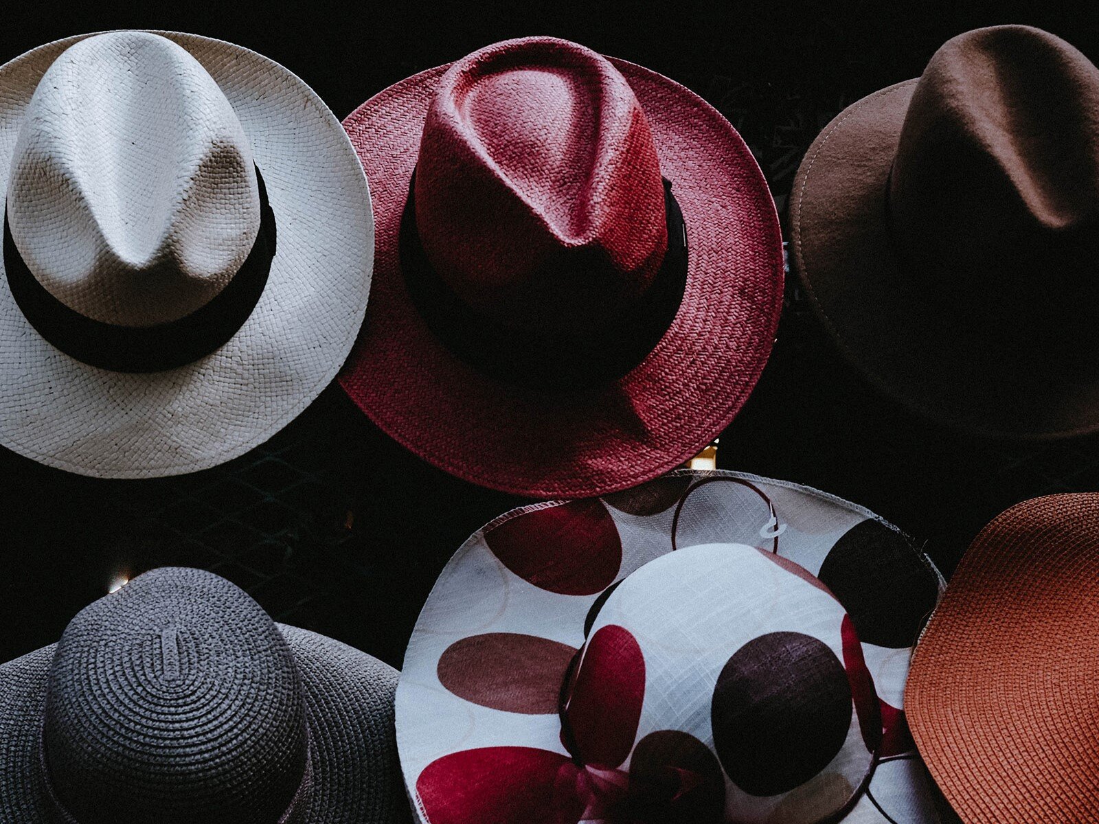 Zdjęcie przedstawia sześć letnich kapeluszy, ułożonych w dwóch rzędach po trzy. W górnym rzędzie widoczne są klasyczne męskie kapelusze w kolorach: białym, czerwonym i brązowym. W dolnym rzędzie znajdują się damskie kapelusze z dużym rondem w kolorach: granatowym, białym w czerwone grochy oraz czerwonym.