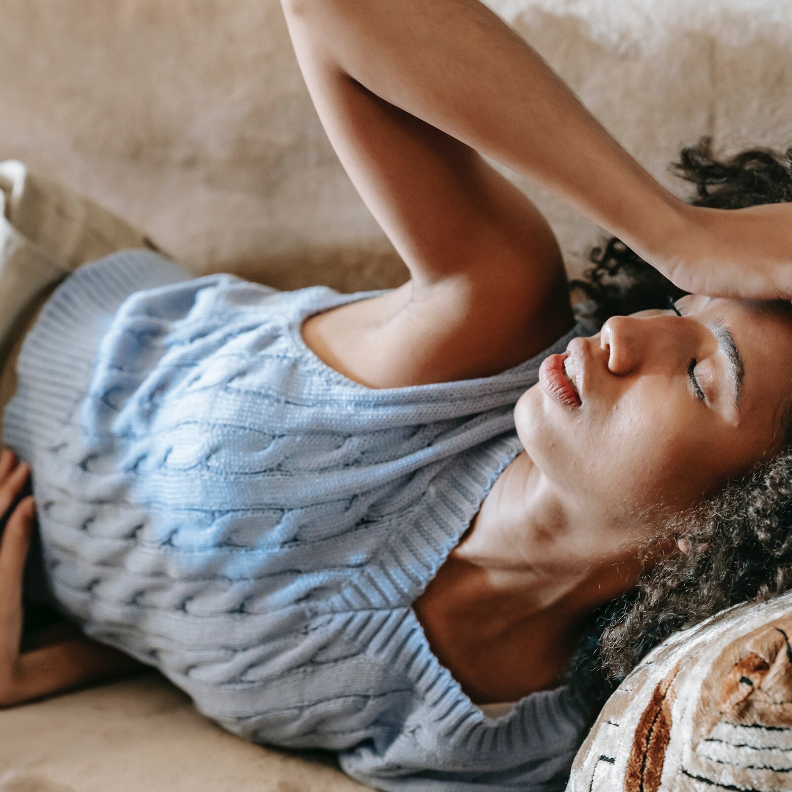 Na zdjęciu widoczna jest kobieta leżąca na kanapie. Na jej twarzy widoczny jest grymas bólu. Kobieta ma zamknięte oczy. Jedną rękę trzyma na głowie, a drugą na brzuchu. 