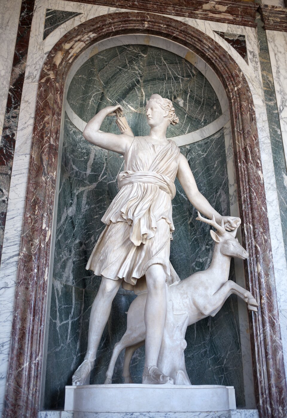 Na zdjęciu znajduje się rzeźba Diany z młodym jelonkiem. Bogini została ujęta w półkroku. To młoda kobieta o kręconych włosach, upiętych z tyłu w kok.  Jest ubrana w tunikę sięgającą jej do kolan. Na stopach ma sandały. Prawą ręką dotyka kołczanu ze strzałami, zawieszonego z tyłu na prawym ramieniu, odwracając przy tym głowę. Lewą  dłonią trzyma jelonka za lewy róg. Zwierzę wyrywa się, stoi na dwóch nogach, przednie podniesione są do góry, do skoku. Stoi w kontrapoście (na jednej nodze opiera ciężar ciała, a druga jest odciążona). Rzeźba stoi na tle marmurowej ściany z wgłębieniem zakończonym łukiem.