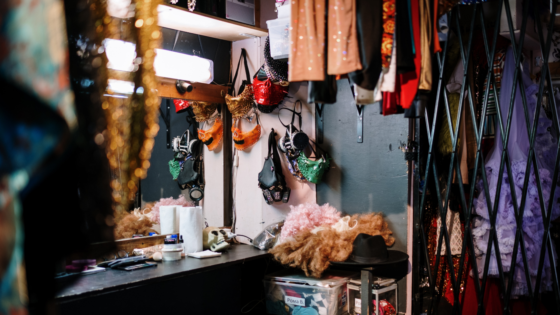 Zdjęcie przedstawia fragment garderoby. Widoczne jest lustro i mnóstwo wiszących dookoła lustra i na ścianie rekwizytów i elementów odzieży.