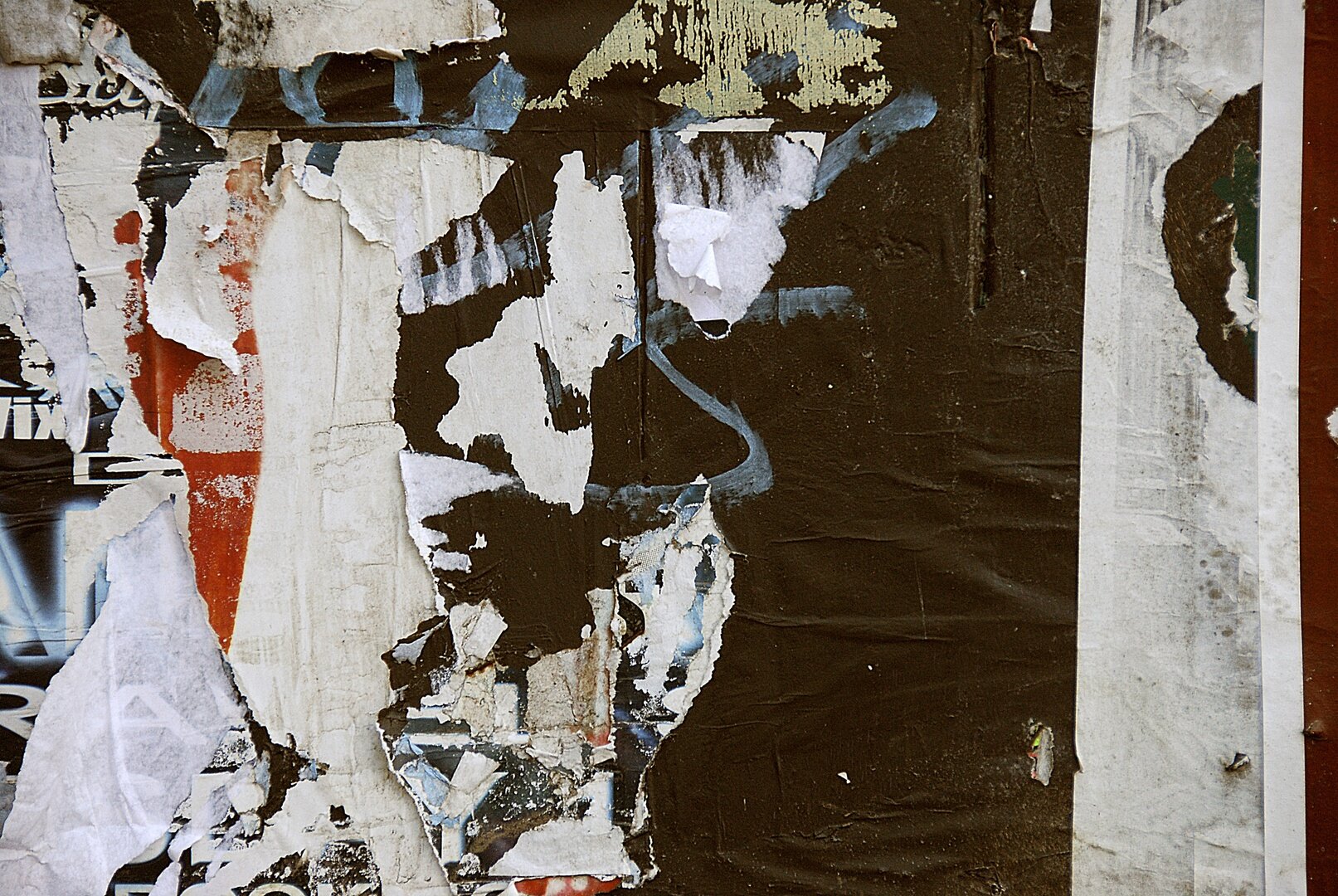 Zdjęcie przedstawia ścianę, na której znajdują się poszarpane resztki naklejonych plakatów.