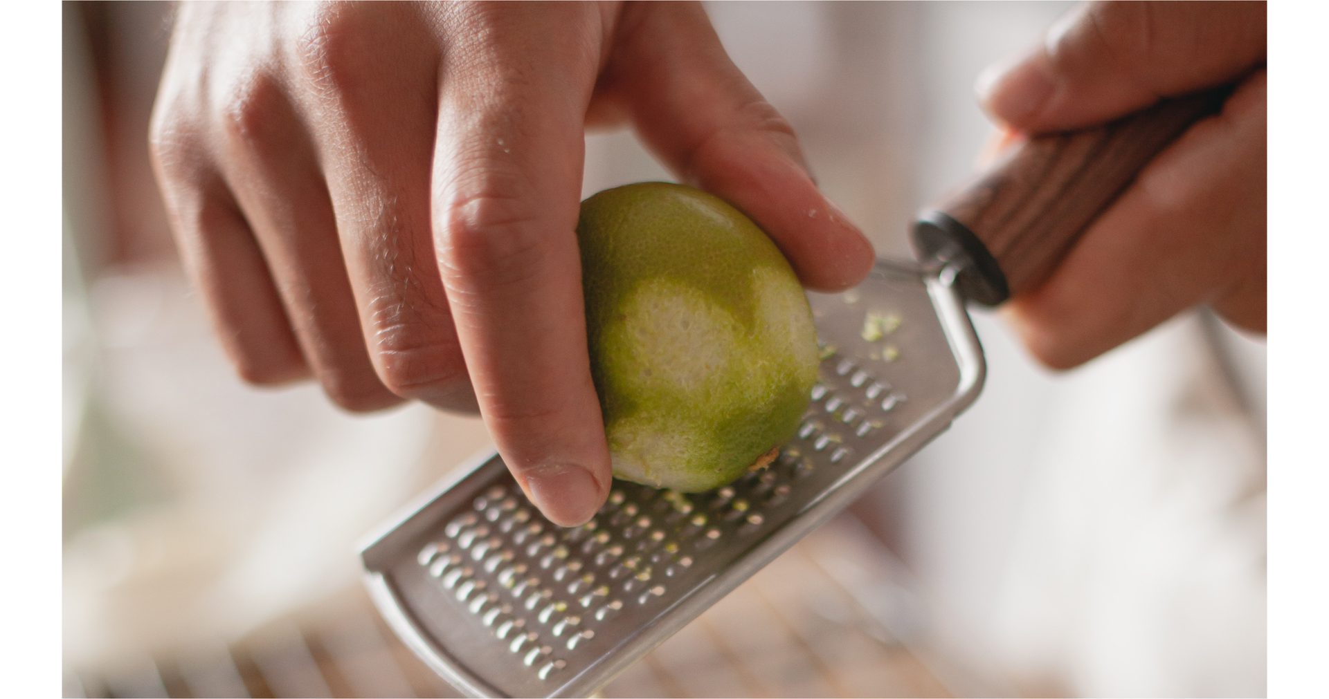 Zdjęcie przedstawia dłonie osoby ścierającej na małej tarce skórkę z limonki.