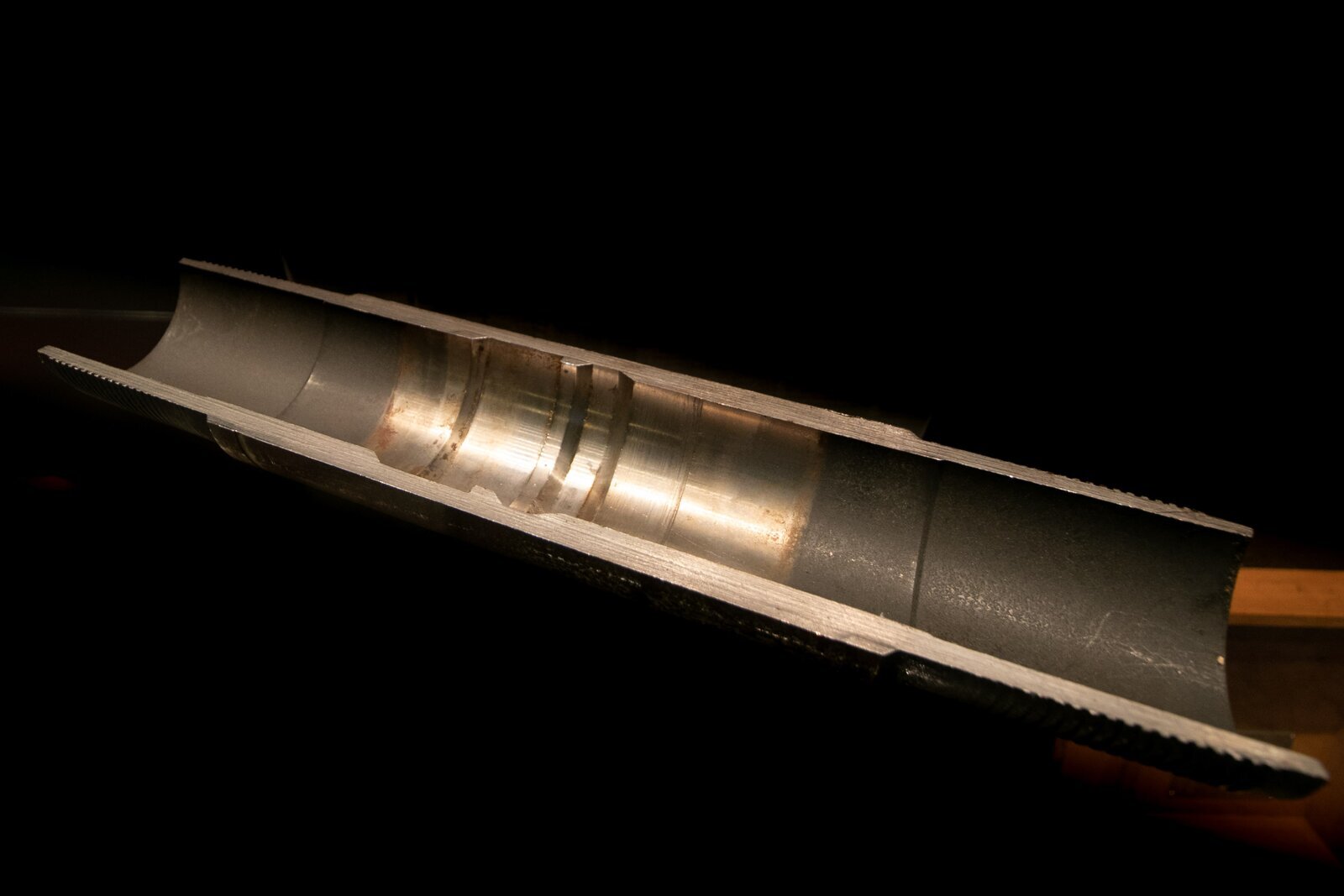 Na zdjęciu widać łącznik posadowy. Łącznik posadowy jest to urządzenie instalowane w kolumnie rur wydobywczych odwiertu w celu posadawiania w nich korków blokujących, zaworów bezpieczeństwa i zaworów wyrównawczych.Łącznik widoczny na zdjęciu jest w kształcie podłużnej rynny. W połowie długości łącznika znajdują się dwa frezy biegnące przez całą jego szerokość. Po obu końcach łącznika na jego zewnętrznych ścianach widać ząbkowanie.