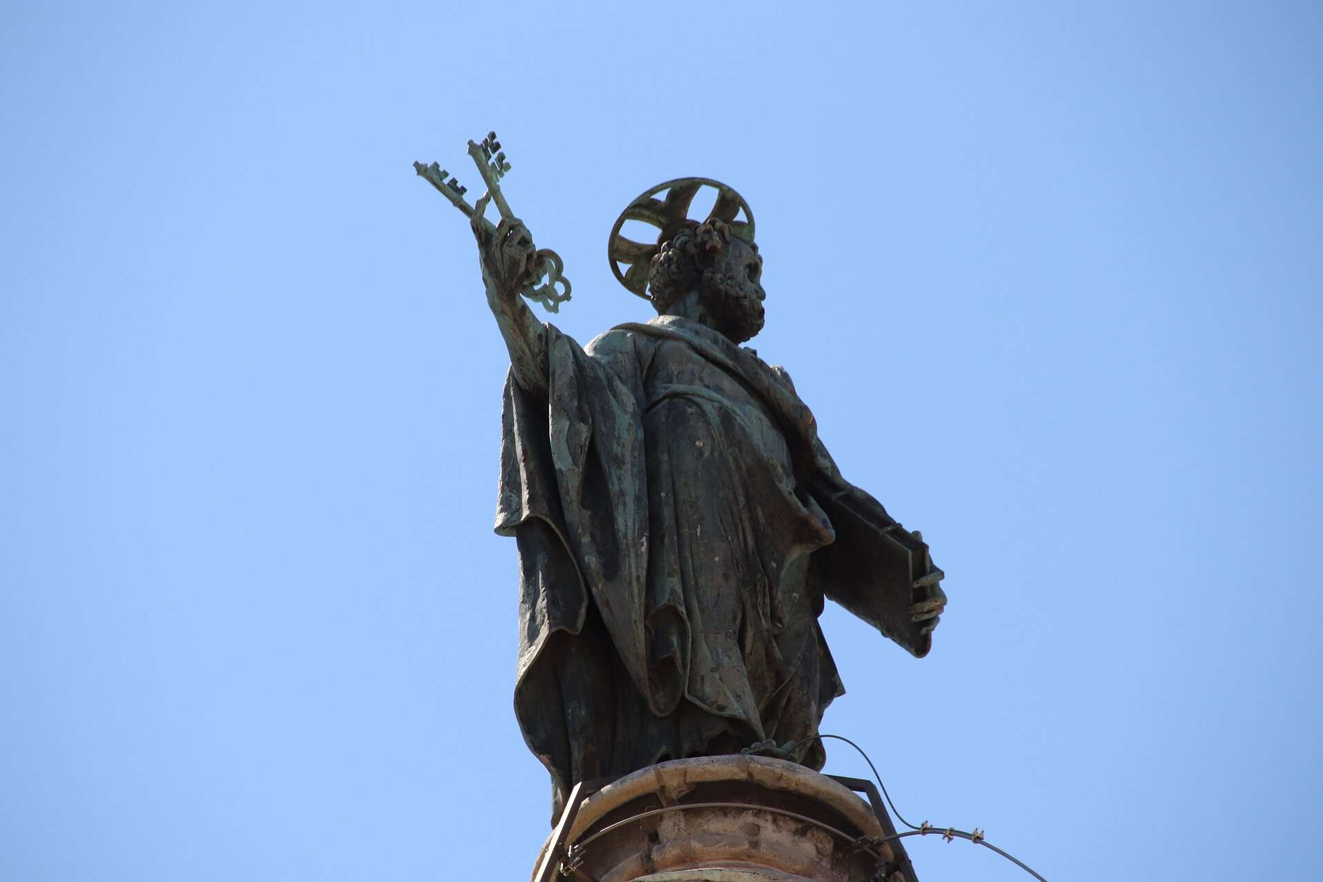 Ilustracja przedstawia fotografię posągu Świętego Piotra - mężczyzny, który trzyma w prawej dłoni dwa klucze, a w lewej księgę. Jest ubrany w obszerną szatę. Nad głową ma aureolę. Rzeźba pokryła się zielonym nalotem.