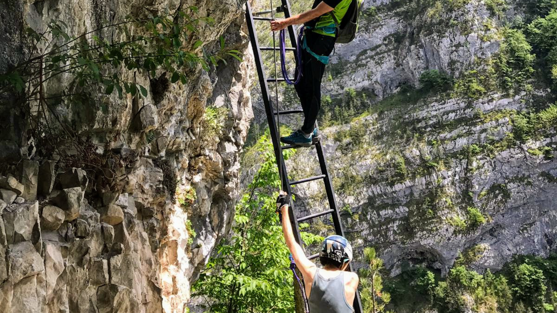 Zdjęcie przedstawia dwie osoby wpinające się po drabince na skałę.