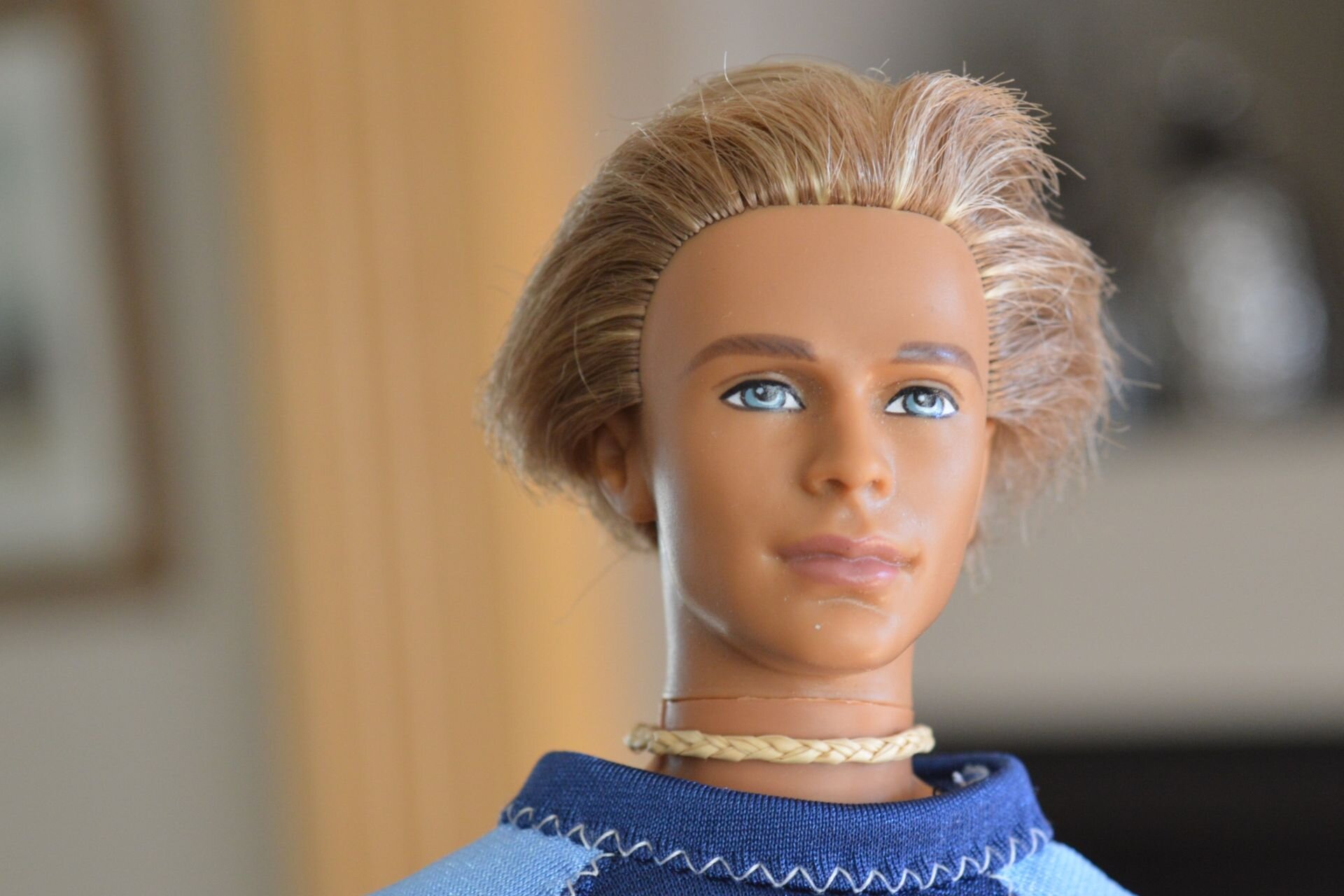Zdjęcie przedstawia lalkę Kena. To szczupły mężczyzna o jasnych włosach i niebieskich oczach.