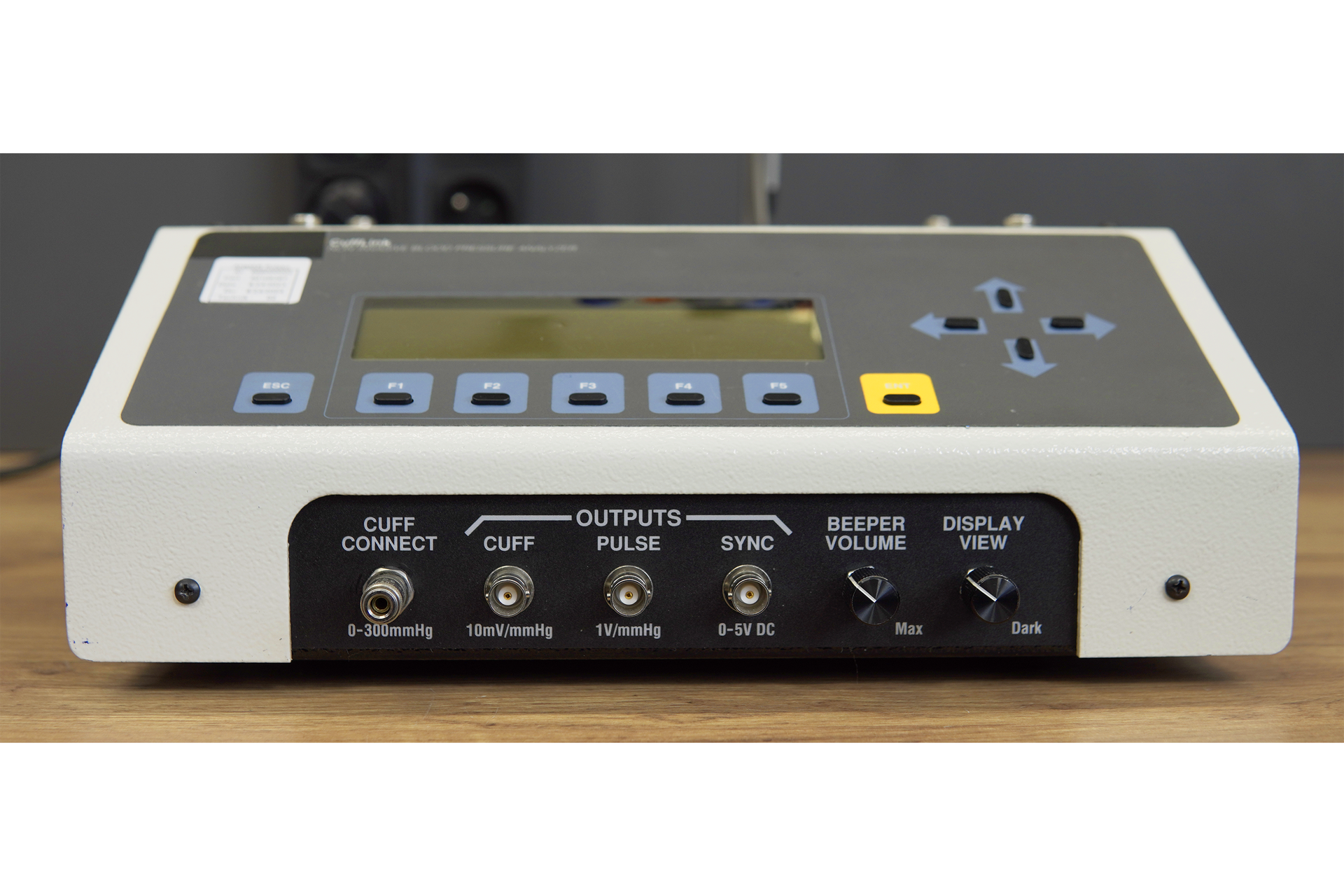 Zdjęcie przedstawia symulator nieinwazyjnego mierzenia ciśnienia tętniczego, w skrócie NIBP w perspektywie od przodu. Na przedniej ścianie obudowy urządzenia znajduje się panel sterujący z przyciskami oraz ekranem. Pod panelem są opisane gniazda do podłączenia urządzeń oraz dwa pokrętła. 