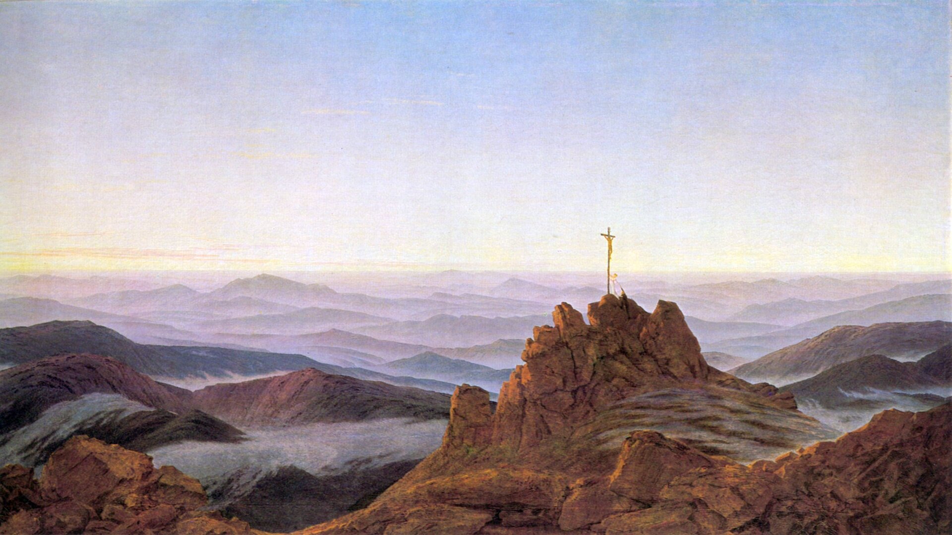 Obraz przedstawia pejzaż górski. Na pierwszym planie znajdują się wysokie skały, na których szczycie stoi krzyż. Wierzchołki gór otoczone są chmurami.