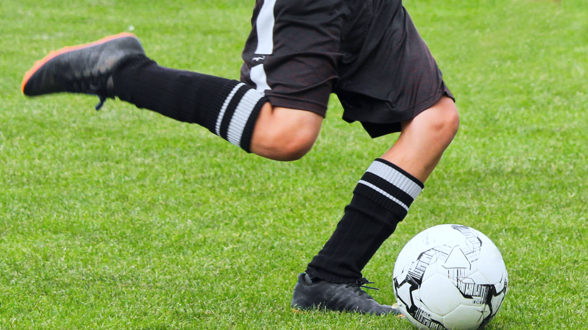 Zdjęcie przedstawia nogi piłkarza zamierzającego się do kopnięcia piłki.