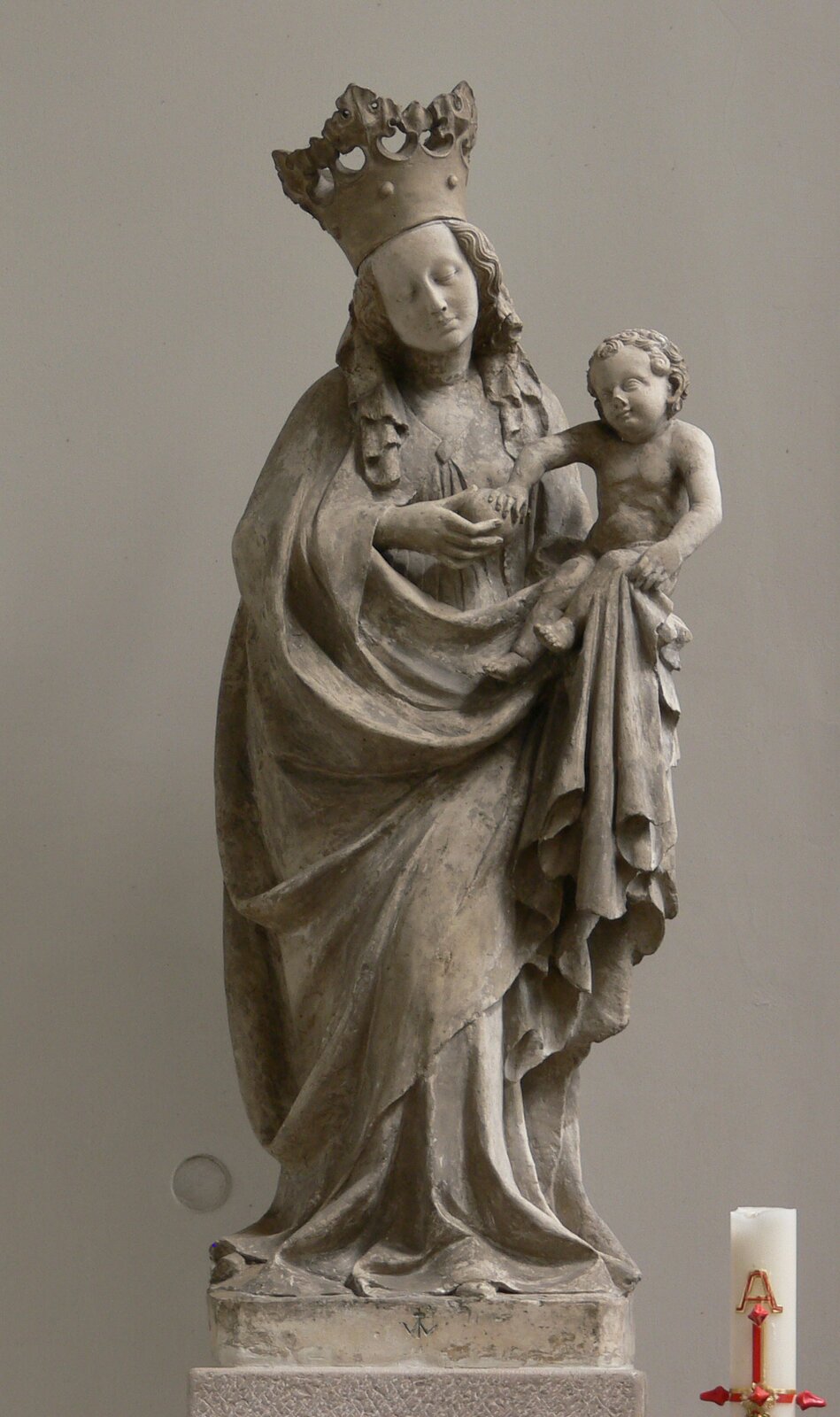 Ilustracja przedstawia rzeźbę „Piękna Madonna z Horb”. Maria stoi na postumencie na szarym tle. Postać wygięta jest w kształcie litery „S”. Na głowie ma koronę. Ubrana jest w suknię, na której ma założony luźny płaszcz. Na lewym ręku trzyma Jezusa, który bawi się jabłkiem trzymanym przez Marię w prawej dłoni. Rysy twarzy Madonny są delikatne. Jej przechylona głowa spogląda na Jezusa. 