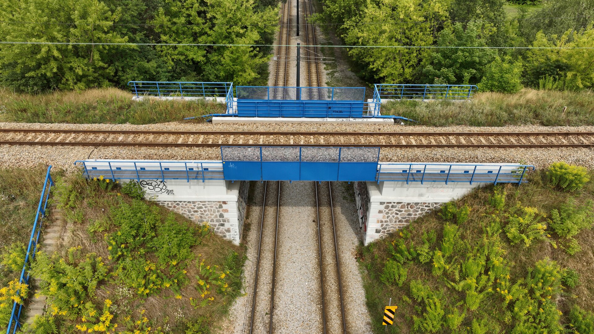 Ilustracja przedstawia wiadukt kolejowy. Zawieszony jest nad dwoma torami tramwajowymi.