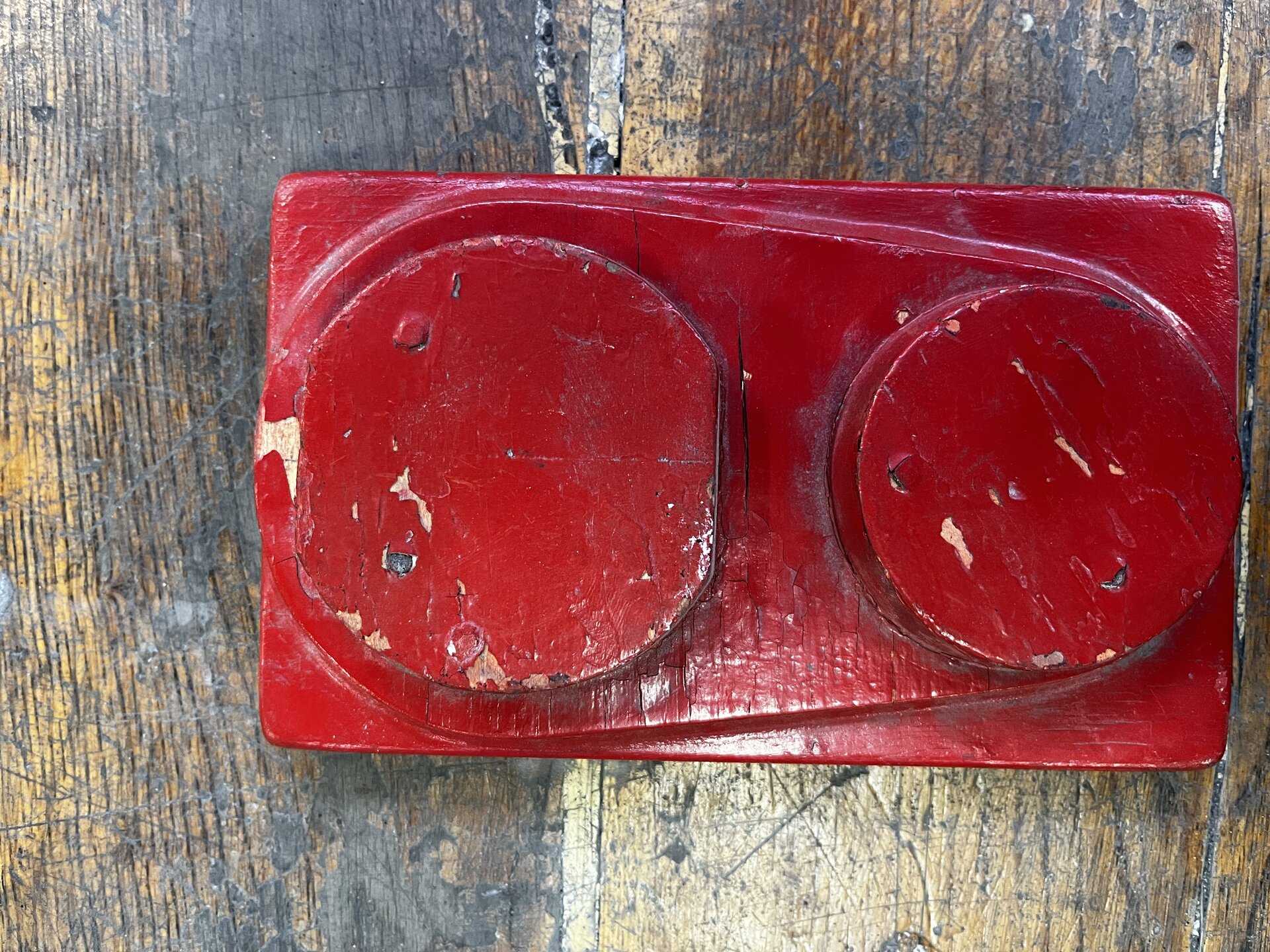 Na zdjęciu pokazano drewniany model odlewniczy z widocznymi pęknięciami. Przedstawiony model jest o kształcie prostopadłościanu. Na dolnej podstawie znajduje się wypukły element o kształcie elipsy na którym osadzone są dwa cylindry. Na powierzchni modelu widoczne są pęknięcia. 