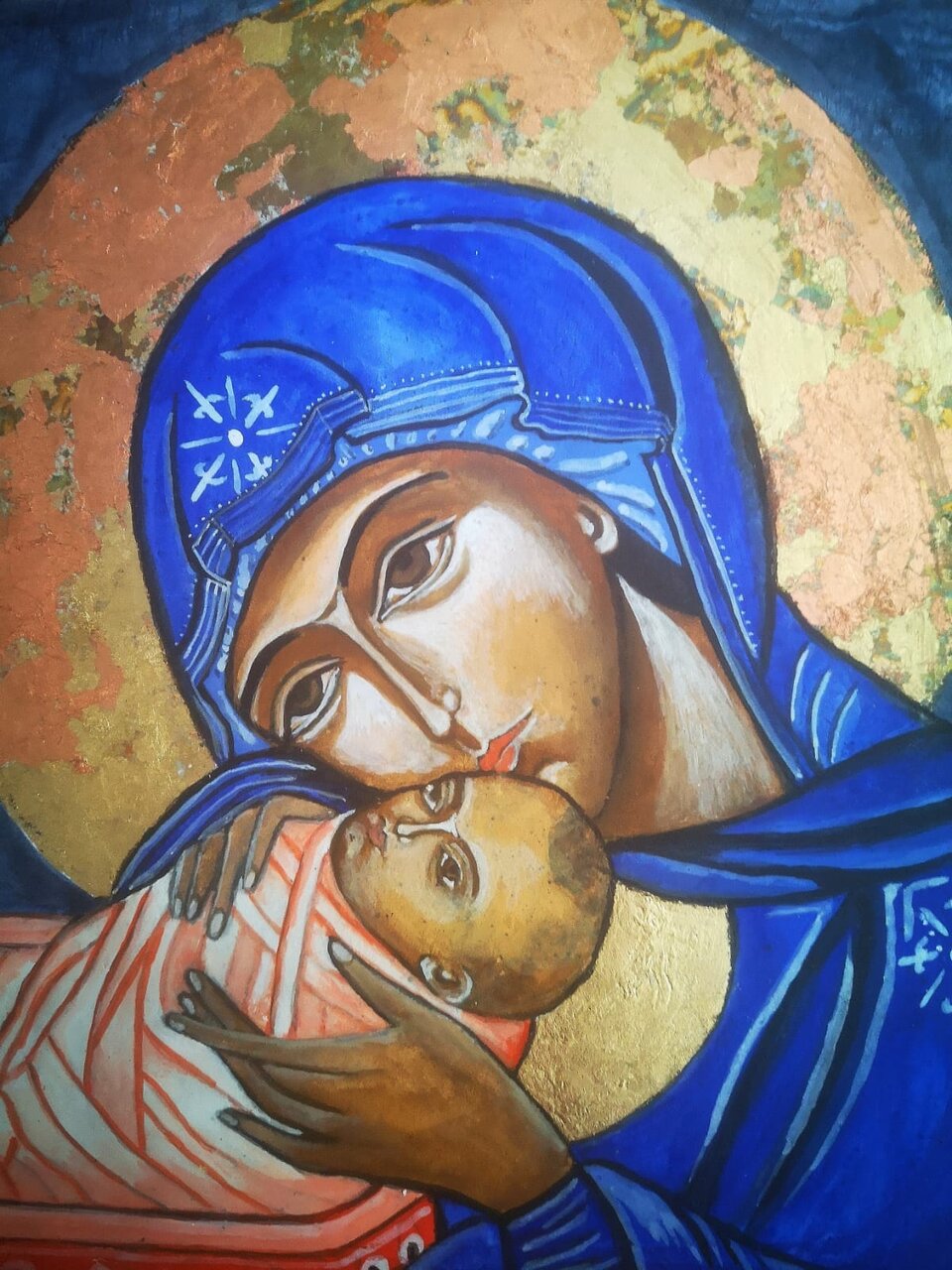 Obraz przedstawia Matkę Boską w chuście na głowie, trzymającą w ramionach niemowlę, Jezusa Chrystusa. Jego ciało jest owinięte w materiał. Kobieta pochyla nad nim głowę. Całuje go w skroń. Nad głową kobiety znajduje się aureola.