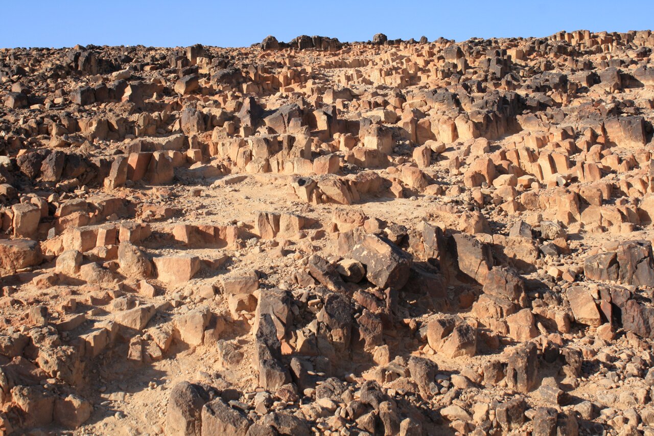 Zdjęcie przedstawia kamienistą powierzchnię pustyni Negev w Izraelu. Wzgórze zajmujące cały kadr zbudowane z kamieniu i piasku ułożonych piętrowo.