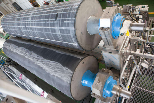 Na grafice przedstawiona jest prasa klejarska. Widoczna jest maszyna wyposażona w dwie duże rolki.