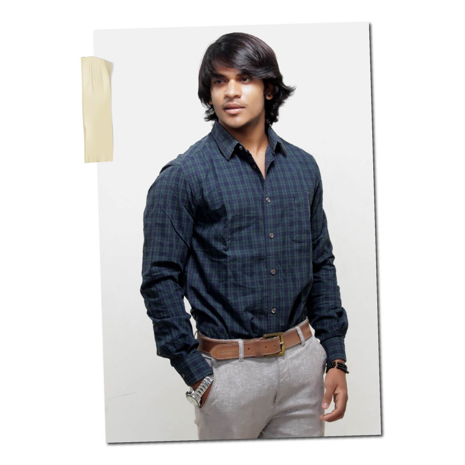 Mężczyzna ubrany jest w koszulę w kratkę oraz jasne szare spodnie. Nosi brązowy skórzany pasek oraz srebrny zegarek.