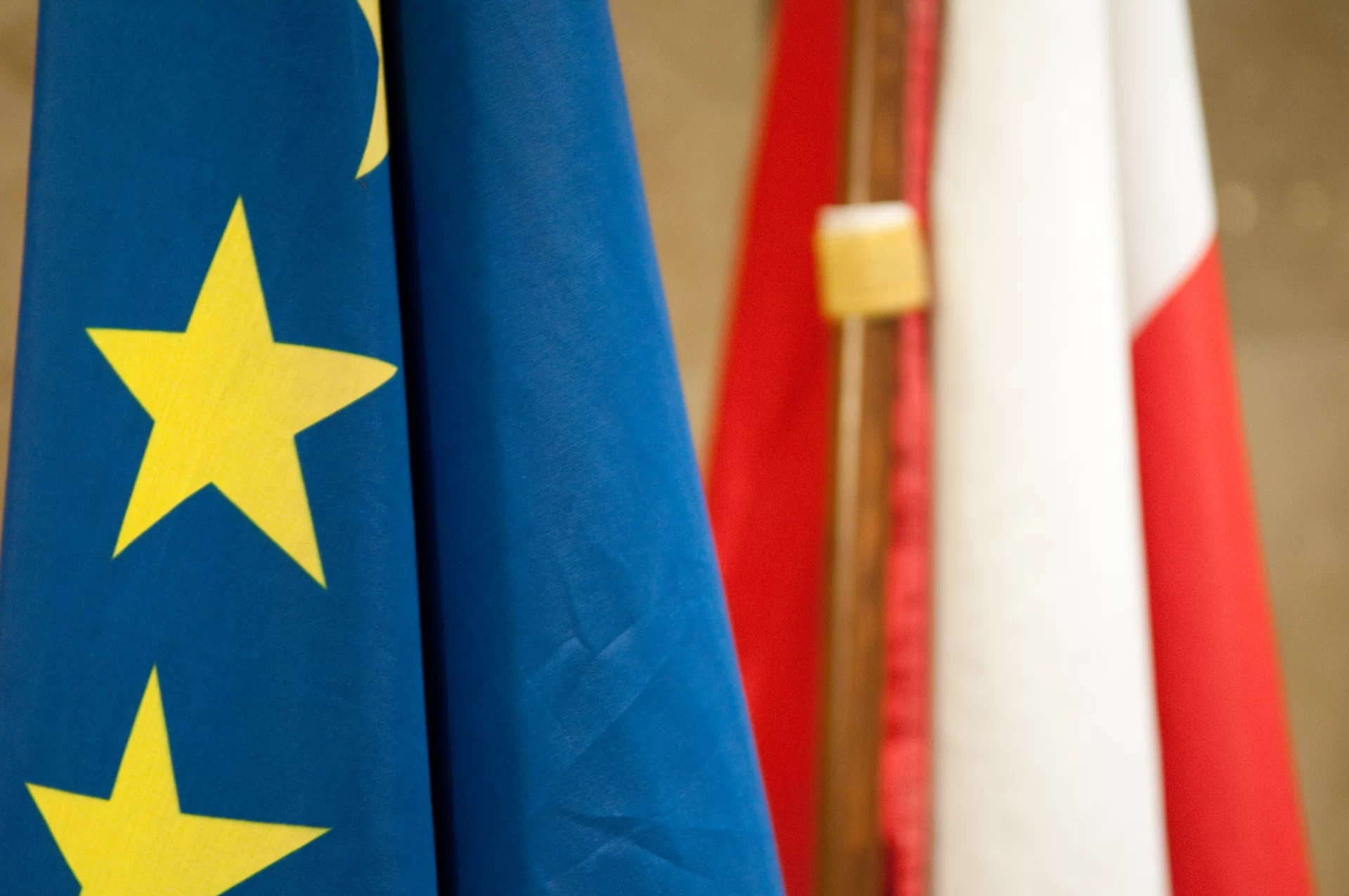 kliknij aby powiększyć Zdjęcie flagi Rzeczypospolitej Polskiej i Unii Europejskiej. Flaga Rzeczypospolitej Polskiej składa się z dwóch pasów: białego i czerwonego. Na fladze Unii Europejskiej widoczna jest gwiazda w kolorze żółtym, która symbolizuje jedność, solidarność i harmonię między narodami Europy na niebieskim tle. Flagi znajdują się w pozycji pionowej.