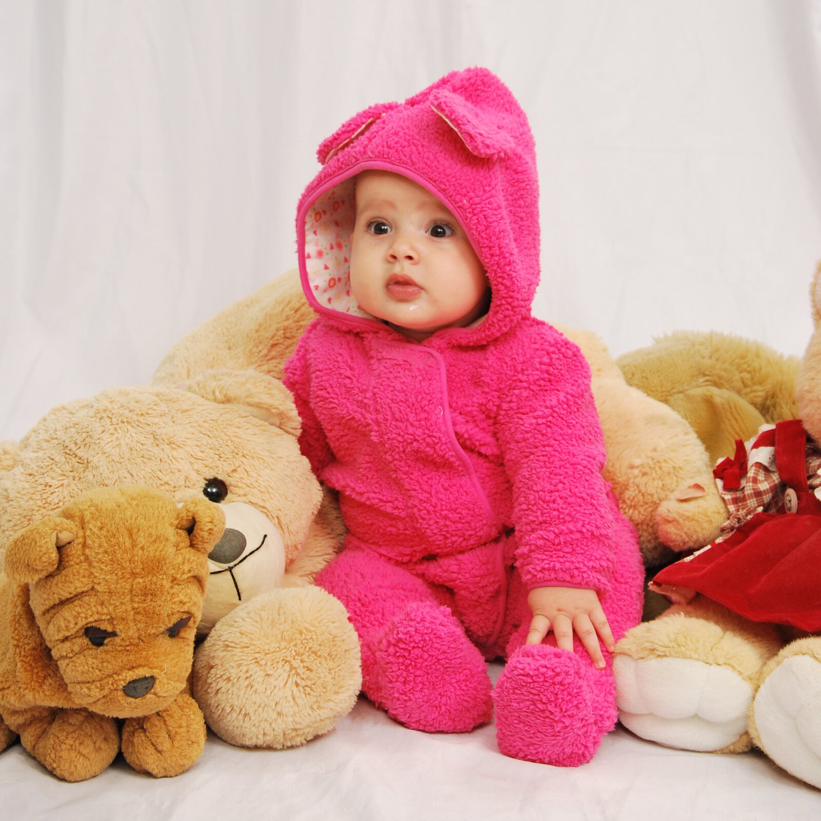 Zdjęcie przedstawia małe dziecko ubrane w różowy kombinezon przytulające się do pluszowego misia. 