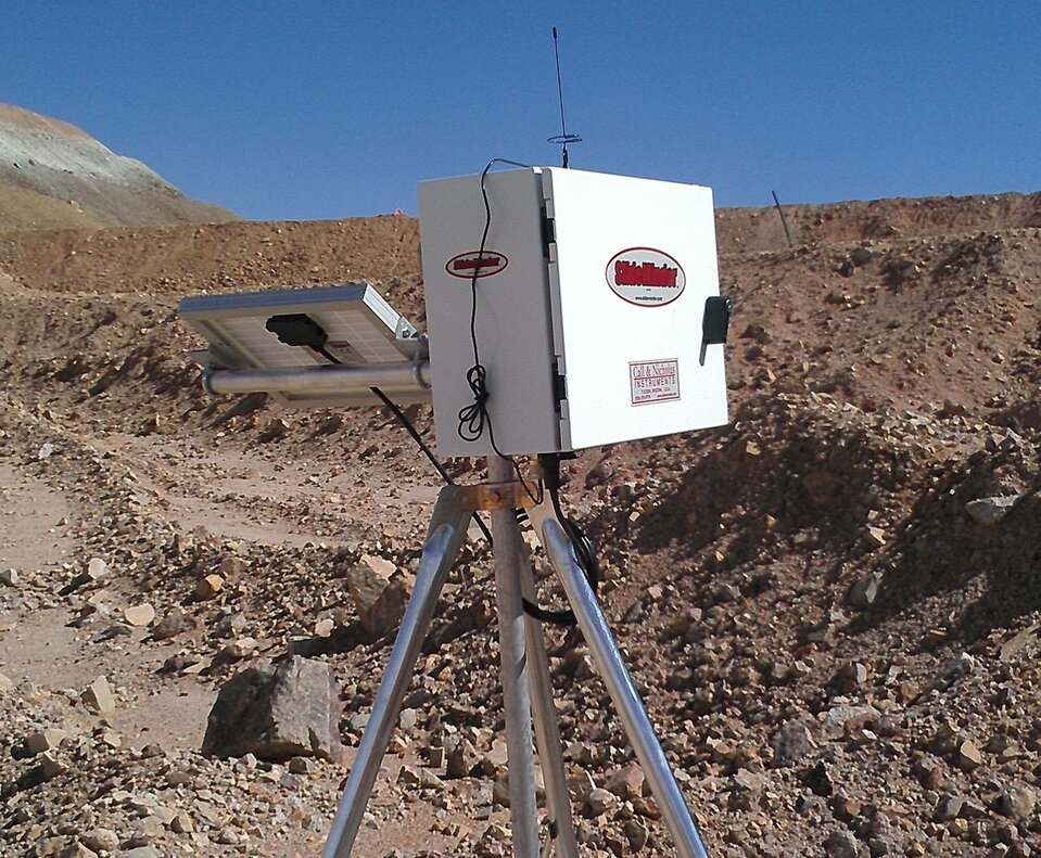 Zdjęcie przedstawia przyrząd monitorujący przemieszczanie się zbocza. Przyrząd stoi na stojaku. Ma postać otwieranej skrzynki oraz baterii słonecznej. Urządzenie stoi w terenie pozbawionym roślinności, skalistym.  