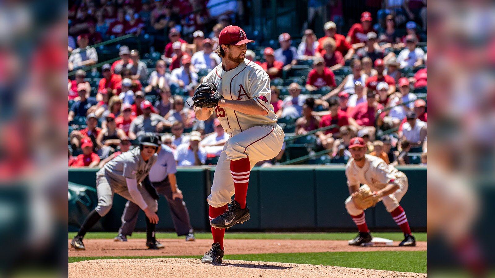 Zdjęcie przedstawia zawodników, uchwyconych w momencie gry w  baseball  . Ubrani są w białe stroje, czerwone podkolanówki i czerwone czapki z daszkiem. Zawodnik znajdujący się na środku zdjęcia ma na ręce rękawicę i przygotowuje się do rzucenia piłki.
