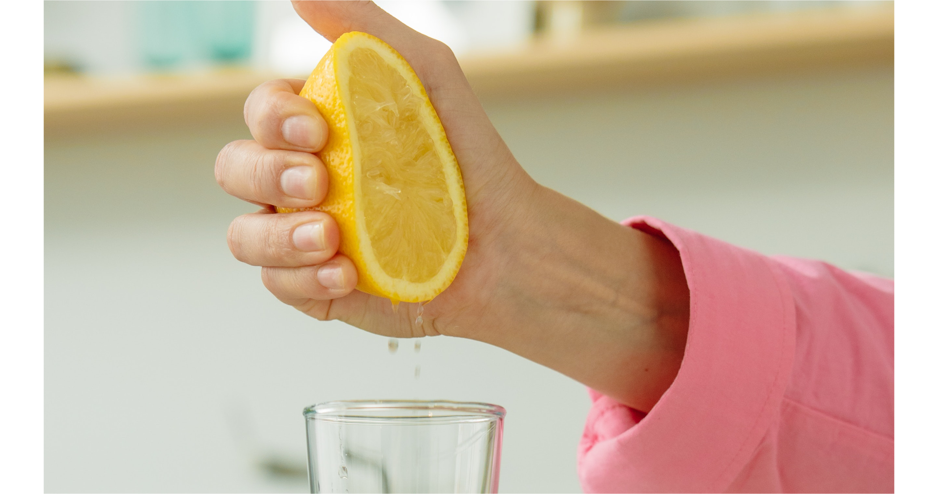 Zdjęcie przedstawia rękę osoby wyciskającej sok z cytryny do szklanki.