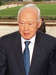 Na zdjęciu znajduje się Lee Kuan Yew, pierwszy premier Singapuru. Mężczyzna jest starszy, ma wschodnie rysy twarzy i skośne oczy. Posiada siwe, krótkie włosy oraz wysokie czoło. Ubrany jest w czarny garnitur, białą koszulę i niebieski krawat w kratkę. 