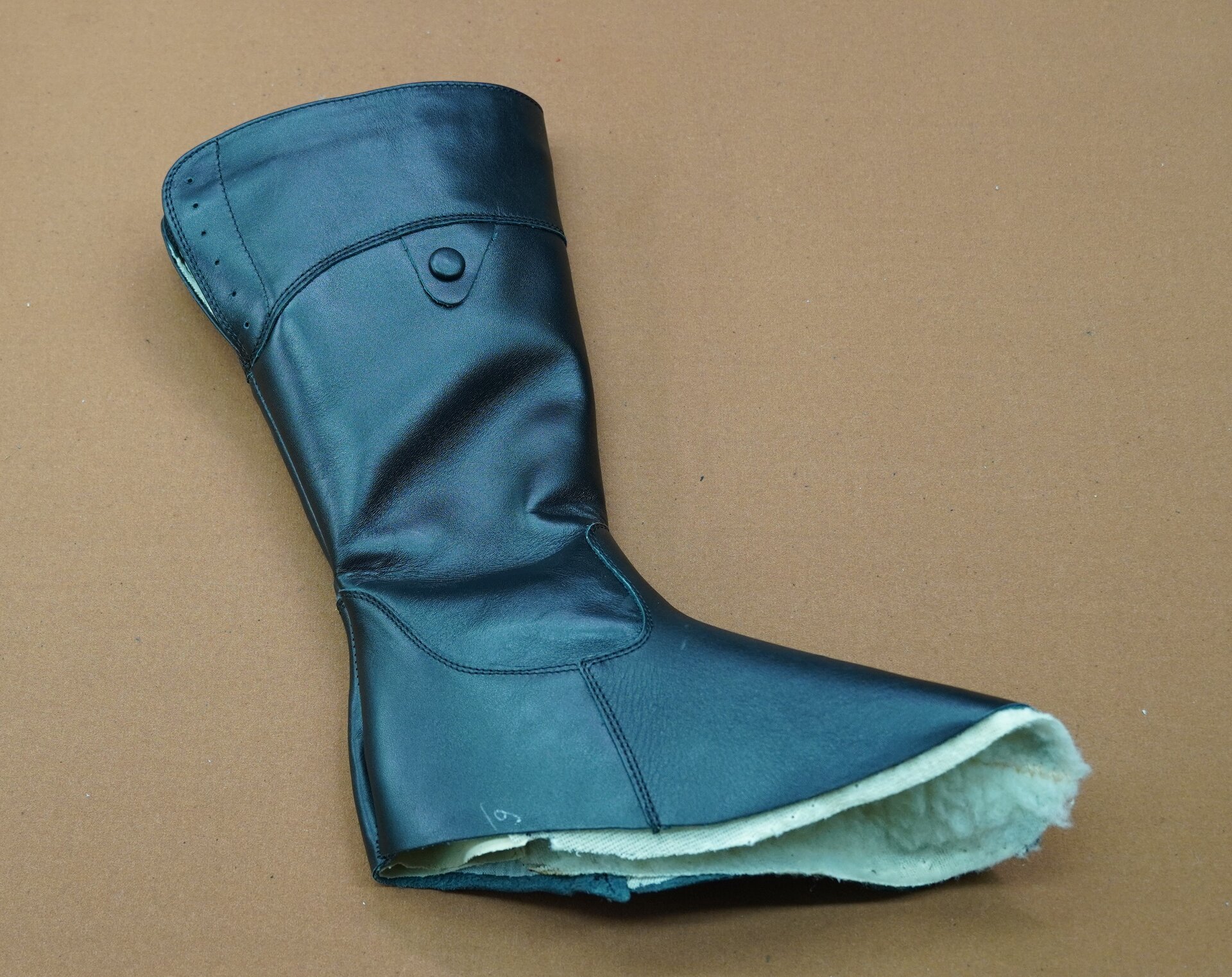 Zdjęcie przedstawia but o wysokiej cholewce leżący na płasko, pozbawiony podeszwy. But jest czarny i skórzany. Nagranie tożsame z treścią.