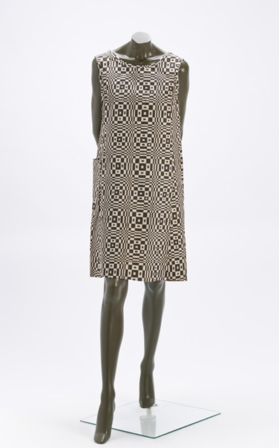 Ilustracja przedstawia sukienkę na manekinie. Sukienka została wyprodukowana przez firmę Paper‑Caper. Sukienka jest przykładem wykorzystania wzorów op‑artu w sztuce użytkowej. Umieszczone są na niej biało czarne wzory.