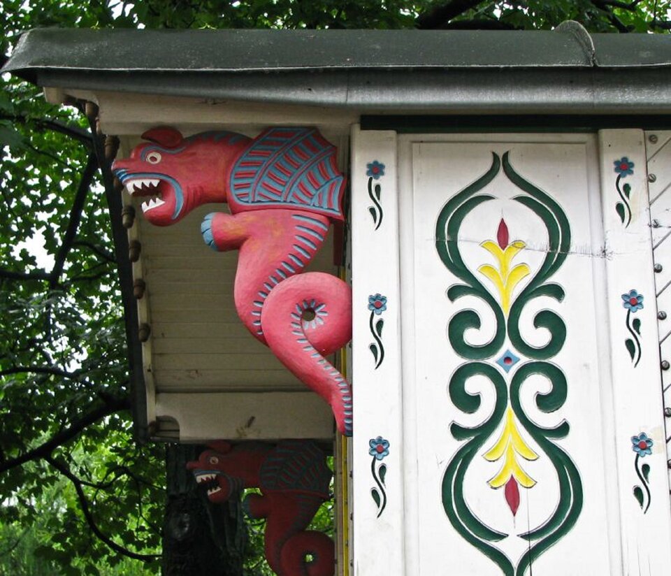 Ilustracja przedstawia ozdobne detale wozu romskiego. Detal to czerwony smok i gryf wykonane z drewna.