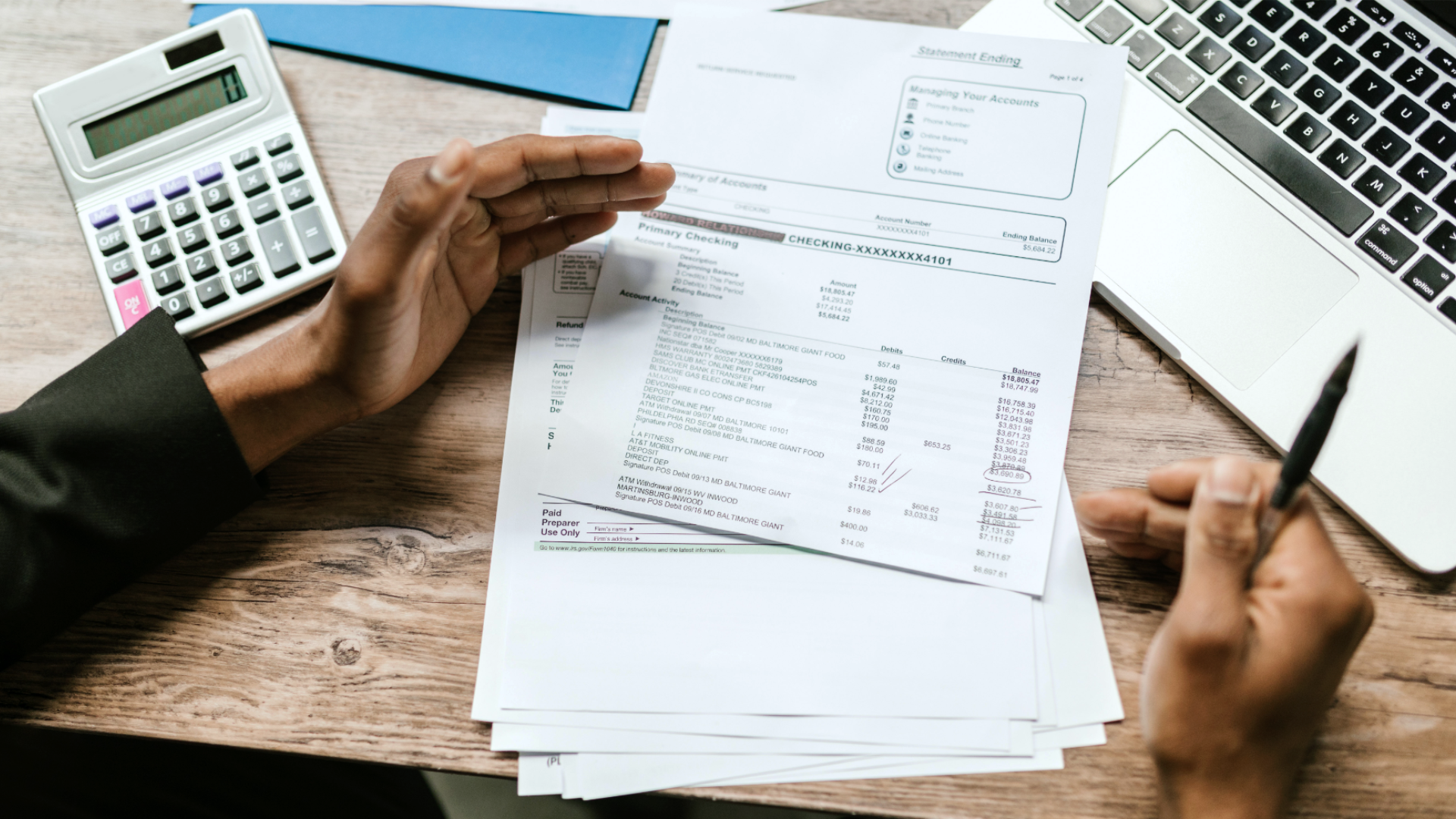 Zdjęcie przedstawia ręce osoby nad fakturami. Obok znajdują się kalkulator i laptop.