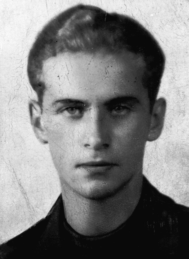 Zdjęcie przedstawia twarz młodego mężczyzny. Jest ona pociągła, nos wydatny, brwi gęste, oczy głęboko osadzone. Mężczyzna ma krótkie, proste, zaczesane ku górze włosy.