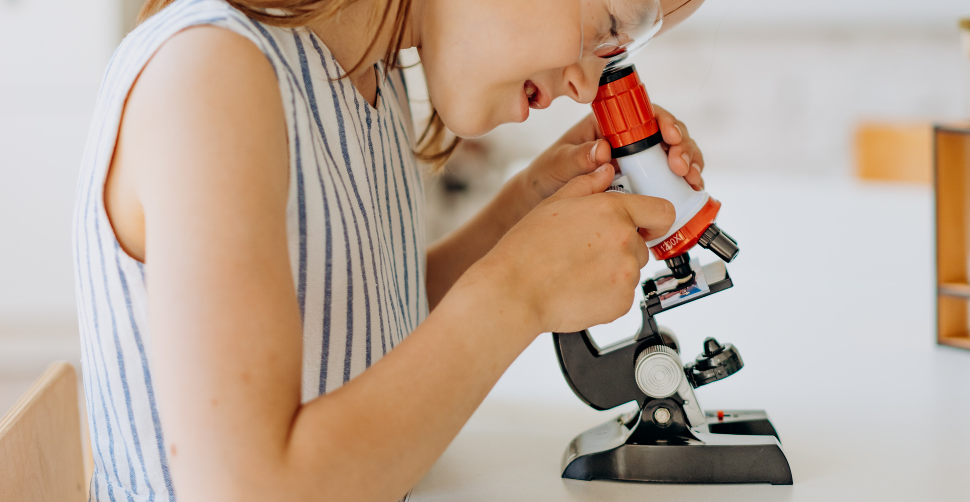 Zdjęcie przedstawia dziewczynę spoglądającą przez mikroskop.