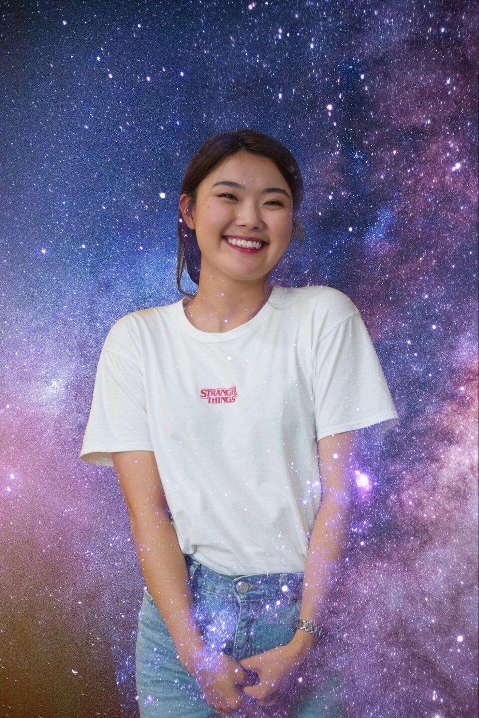 Zdjęcie przedstawia młodą dziewczynę ubraną w białą koszulkę i dżinsy. Ma azjatycką urodę. W tle jest kosmos z licznymi gwiazdami i kolorowym gwiezdnym pyłem. Częściowo postać dziewczyny jest niejako zanurzona w tle.    
