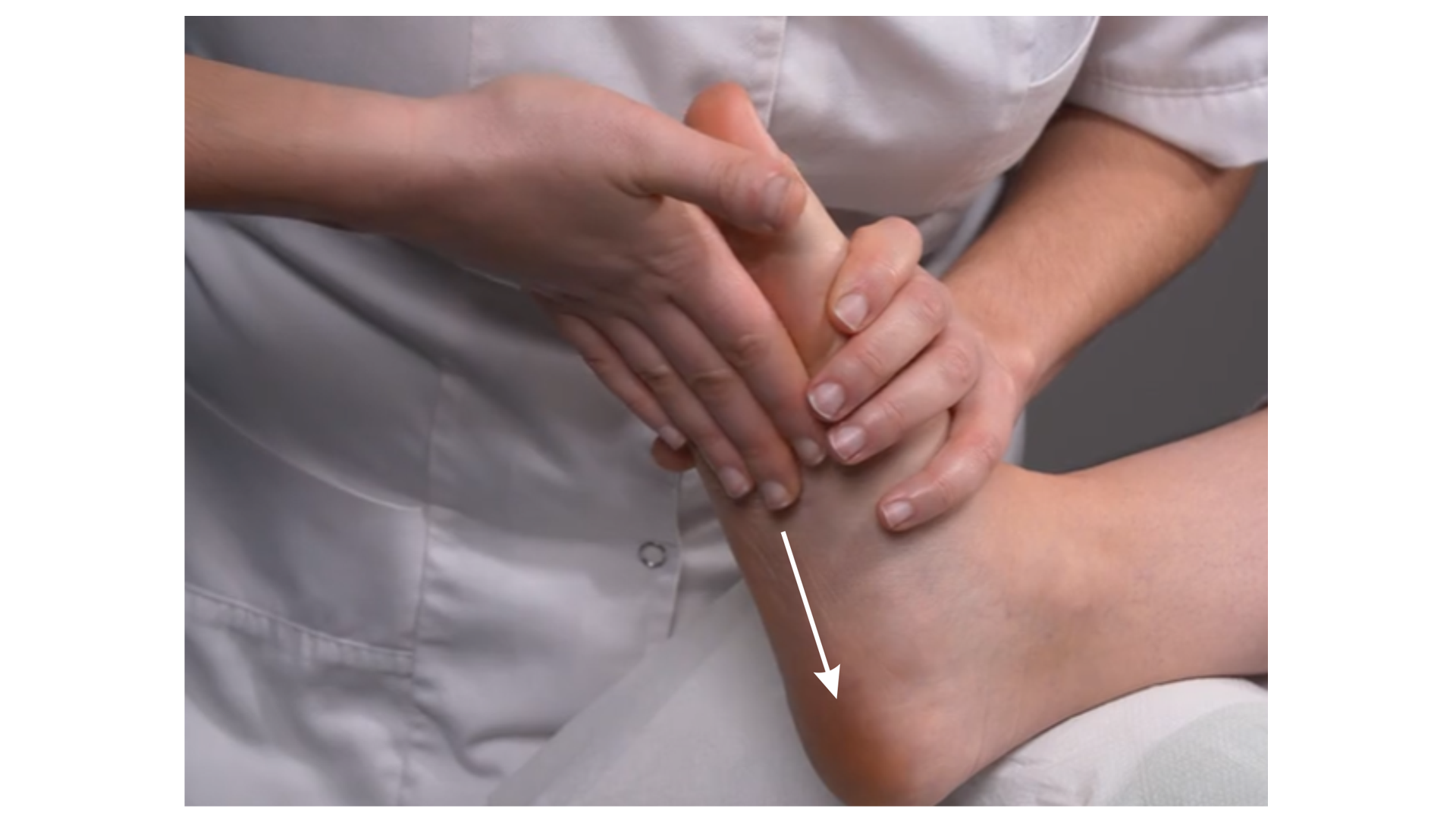 Zdjęcie przedstawia lewą stopę pacjenta leżącego przodem na stole do masażu. Noga pacjenta jest uniesiona powyżej stawu kolanowego. Masażysta wykonuje ruch całą powierzchnią ręki od palców stopy w stronę pięty. Drugą ręką przytrzymuje stopę pacjenta. 