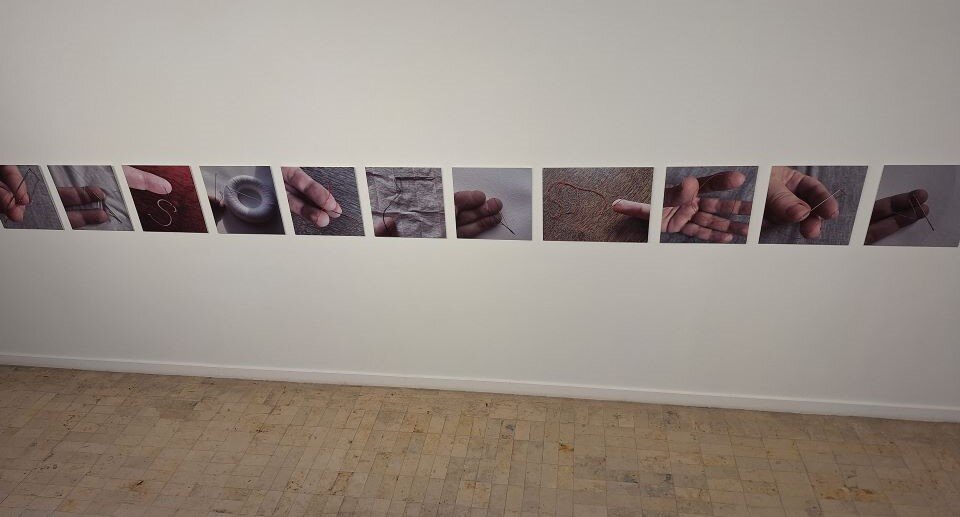 Ilustracja przedstawia fragment wnętrza: białą ścianę i drewnianą podłogę. Na ścianie wisi jedenaście fotografii: tej samej wielkości, w tych samych odstępach i na tej samej wysokości. Tworzą kompozycję rytmiczną i otwartą.