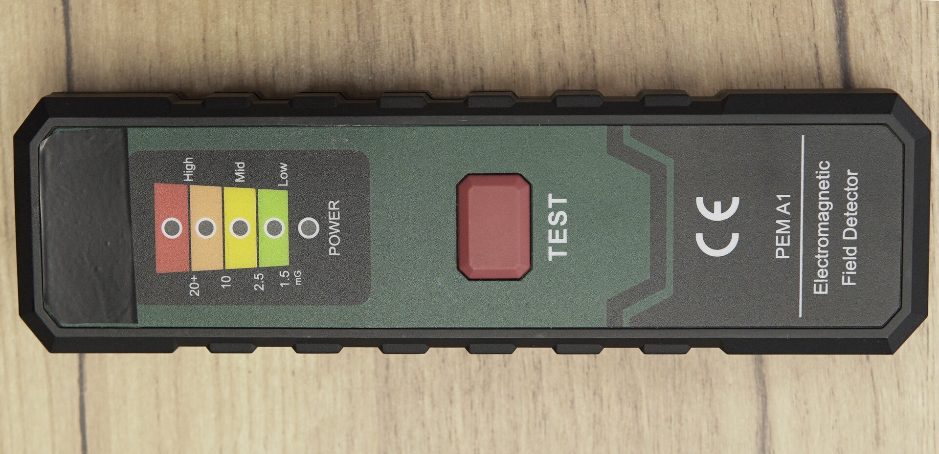 Zdjęcie przedstawia miernik pola elektromagnetycznego. Na górnej ścianie obudowy urządzenia znajduje się czerwony przycisk opisany jako TEST oraz diody informujące o włączeniu urządzenia oraz wielkości natężenia mierzonego pola elektromagnetycznego. 