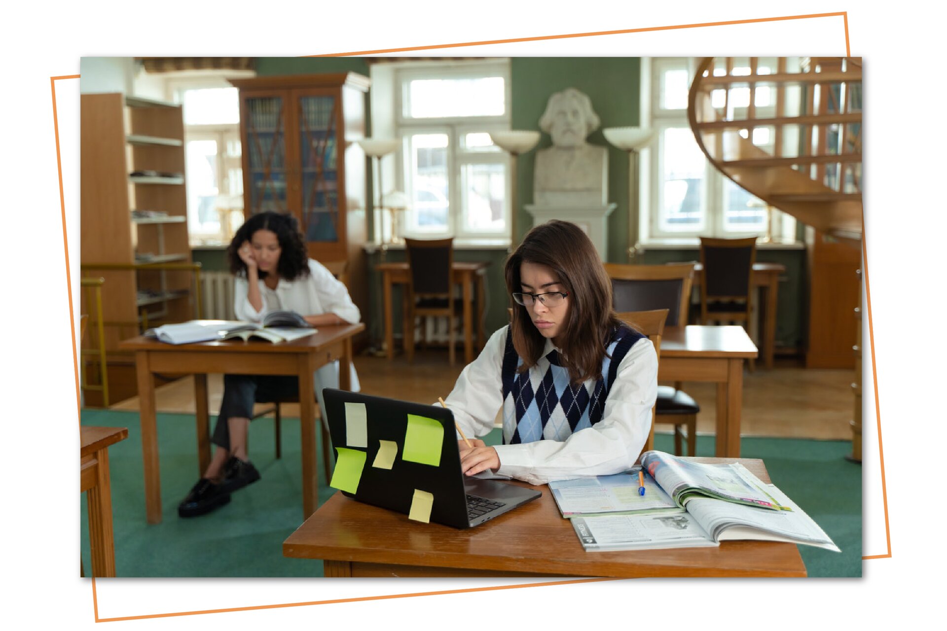 Na zdjęciu widoczne są dwie dziewczyny uczące się w bibliotece. Każda z nich siedzi w pojedynczej ławce. Na obu ławkach leżą otwarte książki, z których uczą się nastolatki. Jedna z dziewczyn dodatkowo korzysta z laptopa. Oprócz dwóch osób w bibliotece nie ma nikogo innego. 