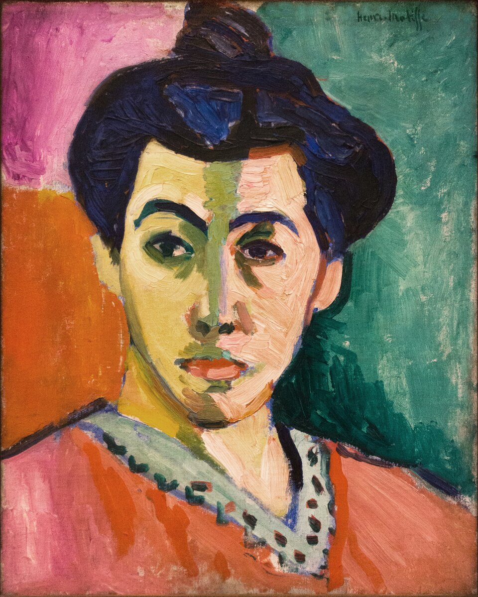 HS‑012‑A-FOTO21 Ilustracja przedstawia obraz Henriego Matisse’a pt. „Portret pani Matisse (z zieloną pręgą)”. Widzimy popiersie kobiety. Ma czarne, upięte włosy, ostre rysy twarzy, duże czarne oczy, ubrana jest w czerwoną sukienkę. Obraz jest namalowany w jednej przestrzeni, zarówno postać kobiety, jak i tło – wszystkie elementy malowane są tą samą grubością farby. Barwy są jaskrawe, nasycone, kontrastowo zestawione. Tło jest różowo – czerwono – zielone. Twarz podzielona jest grubą, zieloną kreską. Jedna część twarzy jest bardziej żółta, druga jasnopomarańczowa.