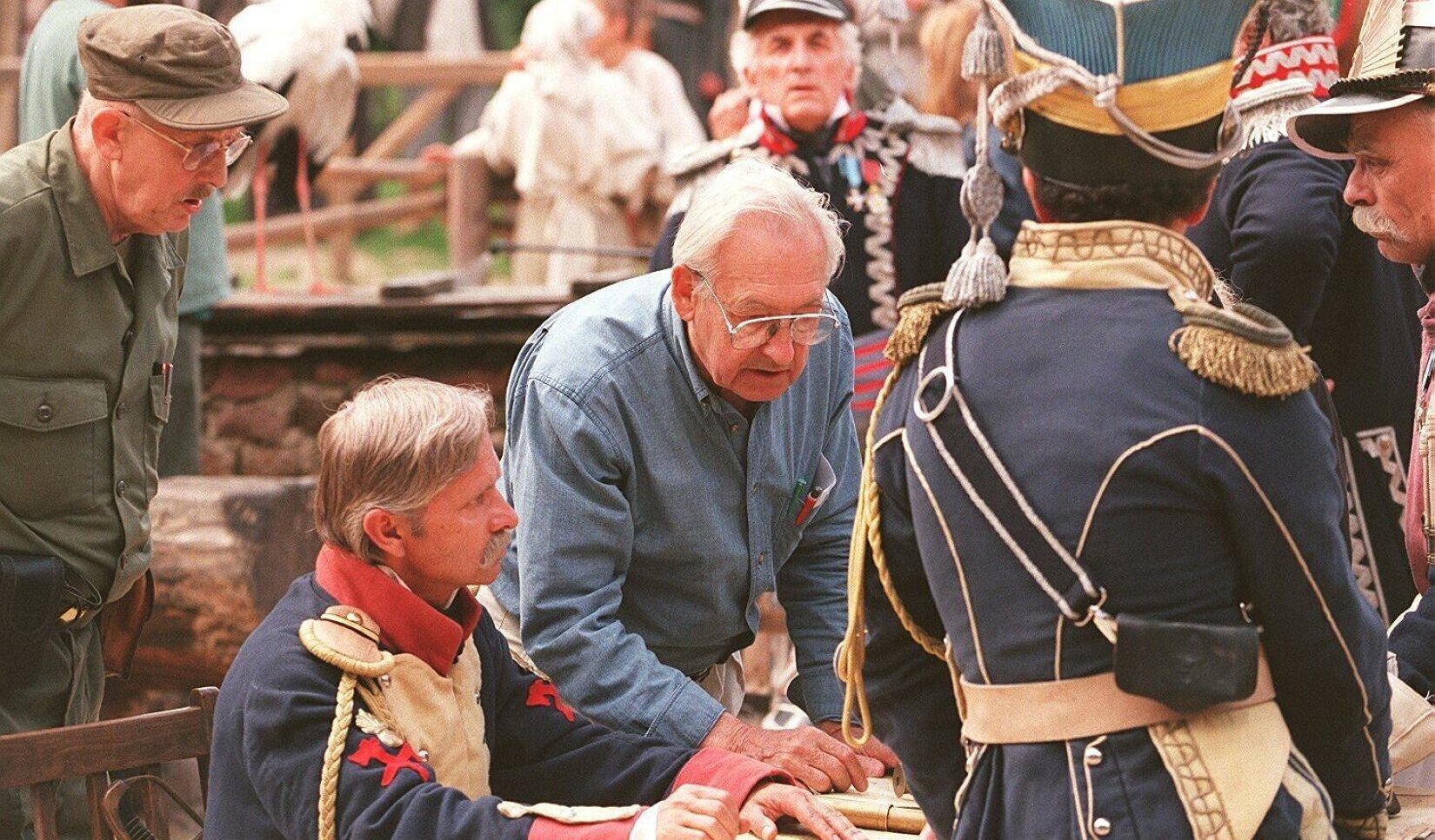 Fotografia przedstawia Andrzeja Wajdę w trakcie prac na planie filmowym. Wajda został sfotografowany jako mężczyzna w podeszłym wieku, o siwych włosach zaczesanych do tyłu. Ubrany jest w niebieską koszulę oraz jasne spodnie. Reżyser pochylony jest nad stołem, na którym znajdują się rekwizyty filmowe. Jest on w centrum ujęcia. Wokół Wajdy zebrała się grupa słuchających go aktorów przebranych w stroje filmowe. Większość z nich ma na sobie mundury w kolorze granatowym z kolorowymi dodatkami. 