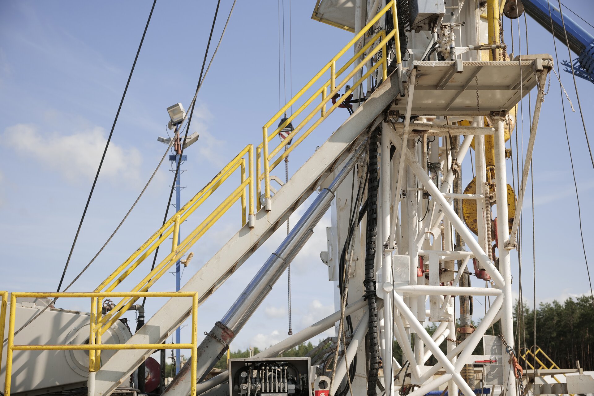 Na zdjęciu widoczny jest proces podnoszenia masztu wiertniczego. Widoczny fragment masztu jest konstrukcją kratową o kształcie prostopadłościanu. Przód masztu jest podparty na podnośnikach hydraulicznych. Podnośniki przypominają pałkę teleskopową wykonaną z trzech wysuwanych cylindrów. Z przodu wieży widoczne są schody zabezpieczone barierką. Schody znajdują się blisko podnośników hydraulicznych.