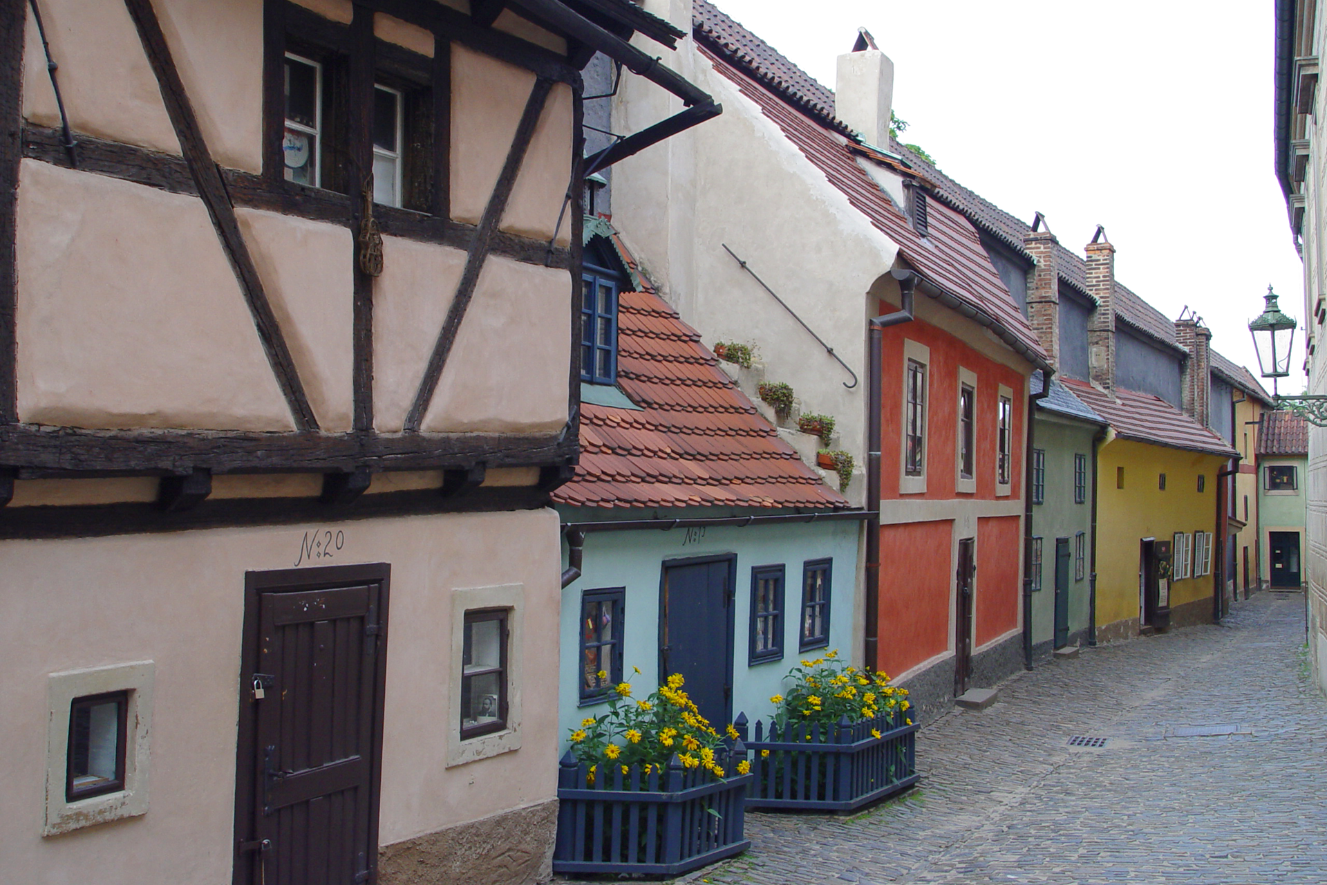 Zdjęcie przedstawia letni widok Złotej Uliczki w Pradze. Jest to miejsce, w którym mieli zamieszkiwać alchemicy i złotnicy na przełomie XVI i XVII wieku. Uliczka zabudowana jest kolorowymi i bardzo małymi domkami. W wąskim kadrze zdjęcia mieści się sześć tradycyjnych budynków mieszkalnych, z których każdy ma inny kolor. Patrząc od lewej: brązowy, turkusowy, czerwony, morski, żółty, jasnożółty i jasnozielony.