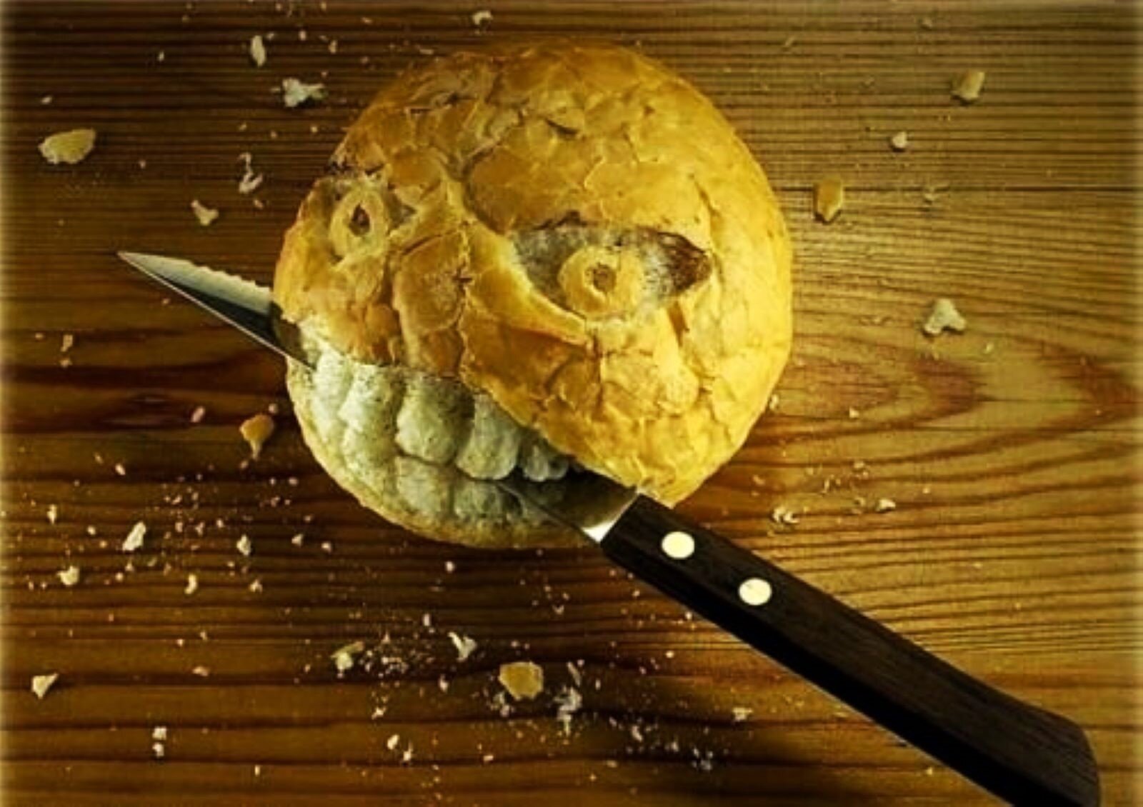Fotografia jest żartobliwa; przedstawia bułeczkę krojoną nożem na desce, która ma wycięte w skórce oczy i szczerzące się zęby. W zębach ma zatknięty nóż. 