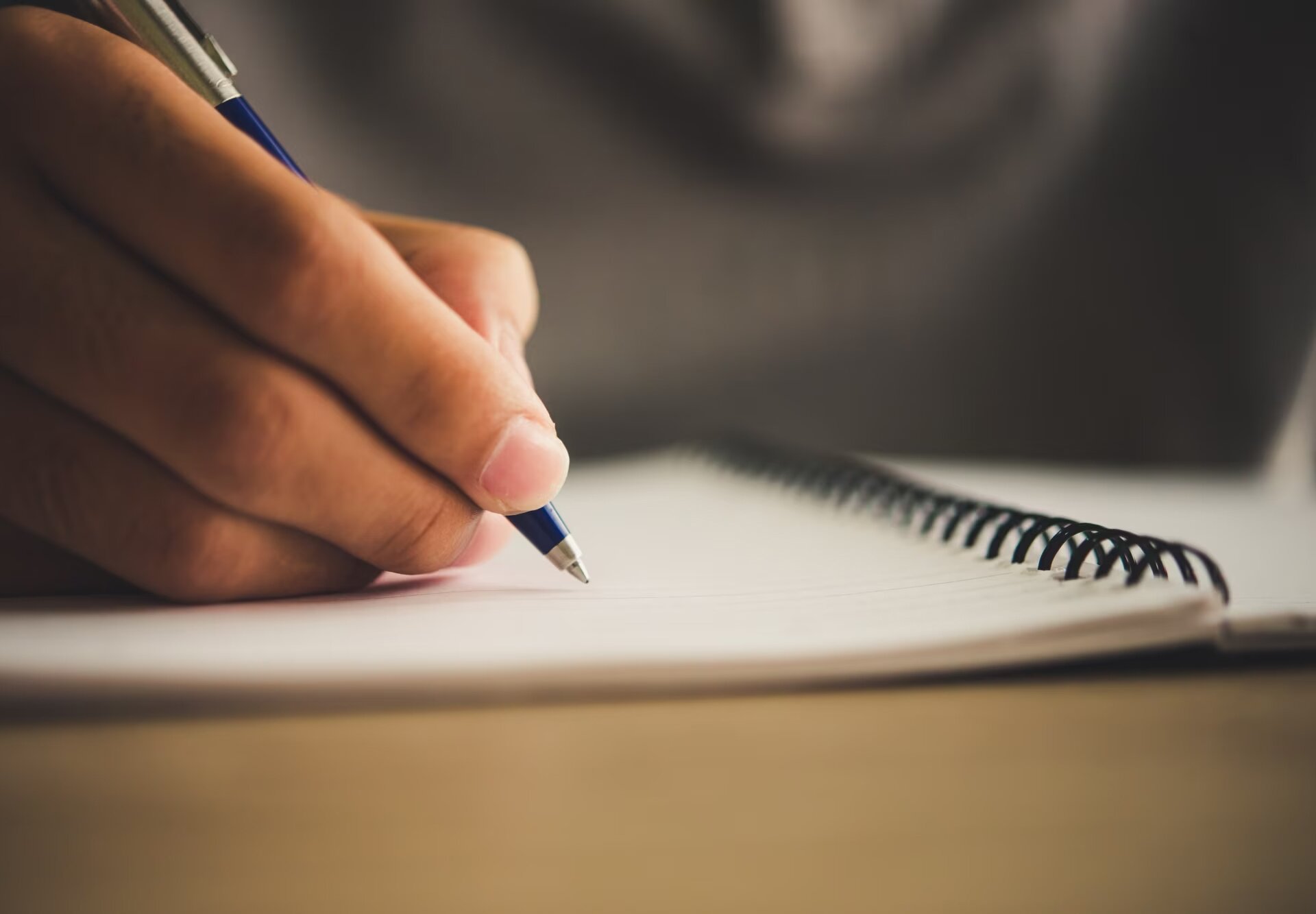 Zdjęcie przedstawia zbliżenie na dłoń trzymającą długopis nad zeszytem.