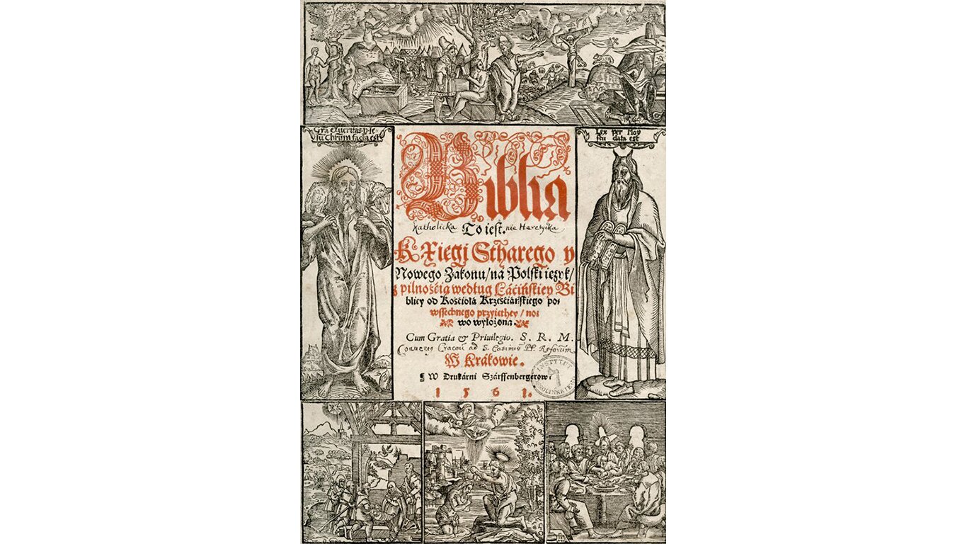 Fotografia przedstawia stronę z jednego z wydań Biblii. Tekst jest bardzo zdobny, czarny i czerwony. Pierwsza litera "b" w słowie "Biblia" została bardzo misternie ozdobiona. Wokół tekstu umieszczono ramkę, która składa się z rycin obrazujących sceny biblijne. The photograph shows a page from one of the editions of the Bible. The text is very ornamented, black and red. The first letter "b" in the word "Bible" has been very elaborately decorated. A frame is placed around the text, which consists of figures depicting biblical scenes.