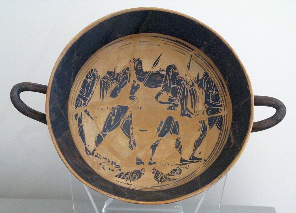 Ilustracja przedstawia antyczne naczynie. Jest to płaska misa z dwoma uszami, wewnątrz naczynia widać  malowidła - postacie wojowników.