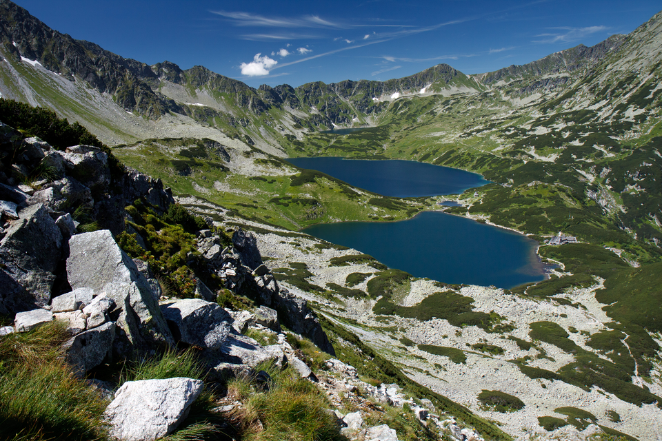 Fotografia przedstawia dwa niebieskie stawy w otoczeniu skał i szczytów gór. To Dolina Pięciu Stawów w Tatrzańskim Parku Narodowym.