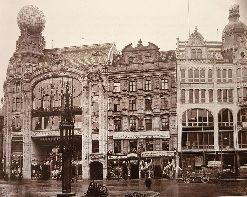 Zdjęcie przedstawia rząd kamienic w mieście. Kamienice są kilkukondygnacyjne. Mają liczne, duże okna. Jedna z kamienic zwieńczona jest dużą kulą. Fasady budynków są zwieńczone zdobieniami, kopułami.  