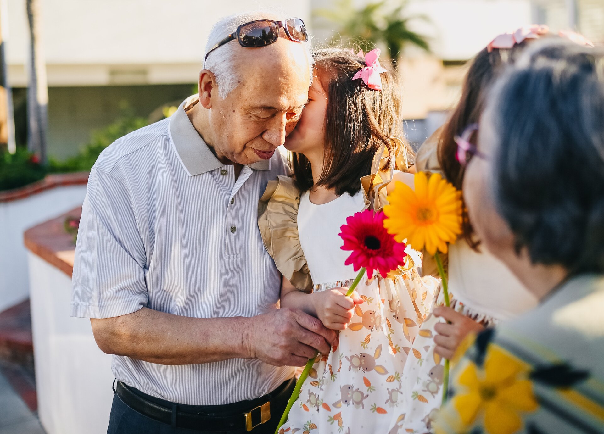 Ilustracja przedstawia starszego mężczyznę wręczającego kwiaty dziewczynce, która całuje go w policzek. 